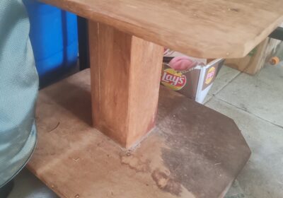 Wooden table with a central support, used for dining or work purposes, in a casual setting.