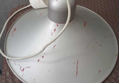 Satellite dish with a white lamp attached, showing signs of wear and paint chipping. Suitable for outdoor or technical use.