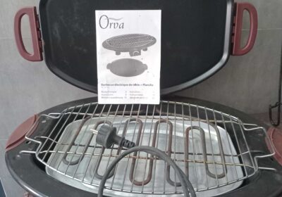 Electric grill with a black lid and red handles, featuring a metal grilling surface and a power cord.