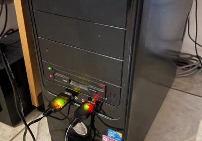 Computer tower with ASUS branding, black color, standard desktop type, connected to power and peripherals, situated on a wooden surface.