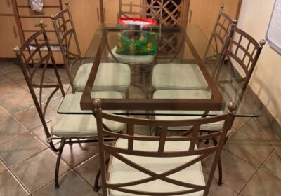 Modern glass dining table with six metal chairs, cream cushions, in a cozy kitchen setting.