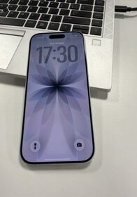 Smartphone with blue floral wallpaper, black frame, and front camera, placed on a silver laptop keyboard.