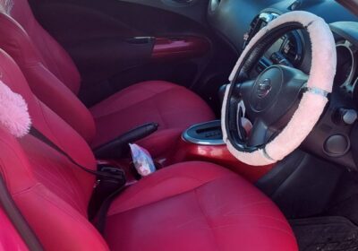 Pink compact car with black interior, featuring a manual transmission and cloth seats, parked outdoors with greenery in the background.