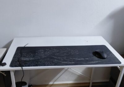 Compact white desk with black mouse pad and computer mouse, situated against a plain white wall in a room with patterned tile flooring.