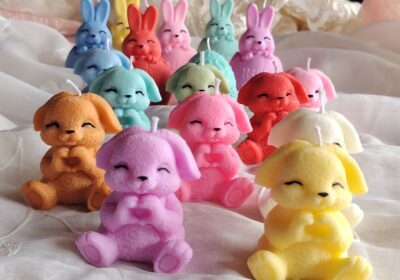 Cute colorful bunny-shaped plush toys for children, in various pastel shades, displayed on a soft fabric surface.