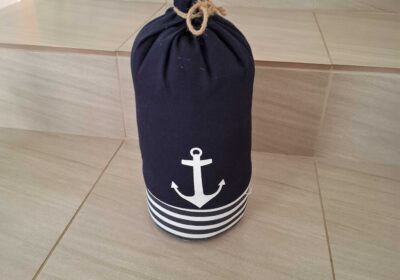 Boat-shaped fabric bag with navy blue color, white anchor design, and striped base, ideal for storage or decor.