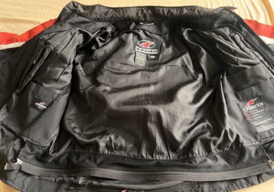 Motorcycle riding jacket with black exterior and red accents, multiple pockets, and protective padding. Ideal for safety and style during rides.
