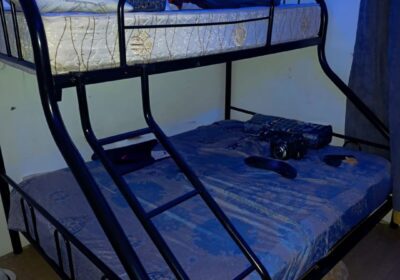 Compact black metal bunk bed with blue and white bedding, suitable for kids or teens. Durable frame with ladder for easy access to the top bunk.