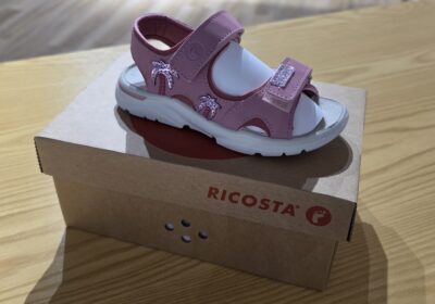 Children’s pink and white sandals with adjustable straps and a small decorative bow.